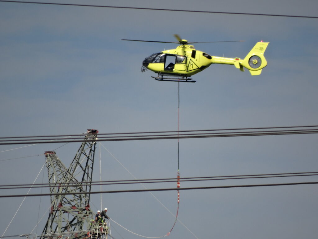Die Kabel einer Stromtrasse werden Hubschrauber von Mast zu Mast gezogen